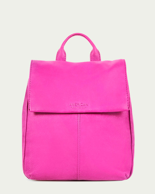 The Liberty Backpack by American Leather Co. is a bright pink women's leather backpack made from genuine American leather. It features a flap closure, top handle, embossed text, minimalist design with clean lines, adjustable straps, and a smooth texture against a solid light grey background.