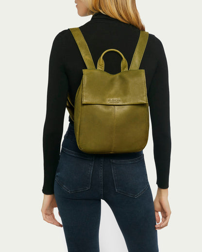 A person in a black long-sleeve shirt and dark jeans is shown from behind, wearing the Liberty Backpack by American Leather Co. Made of genuine American leather, this women's green leather backpack features a handle and two adjustable straps, perfectly complementing their long blonde hair.