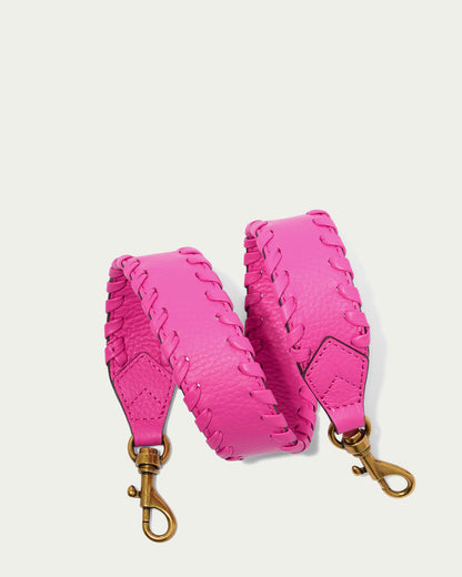 The Luca Strap, a coiled, bright pink leather bag strap from American Leather Co., features decorative stitching along the edges. Made from pebble leather, it has gold-tone metal swivel clasps on both ends for easy attachment to Luca crossbody or other compatible bags. The background is a plain off-white color.