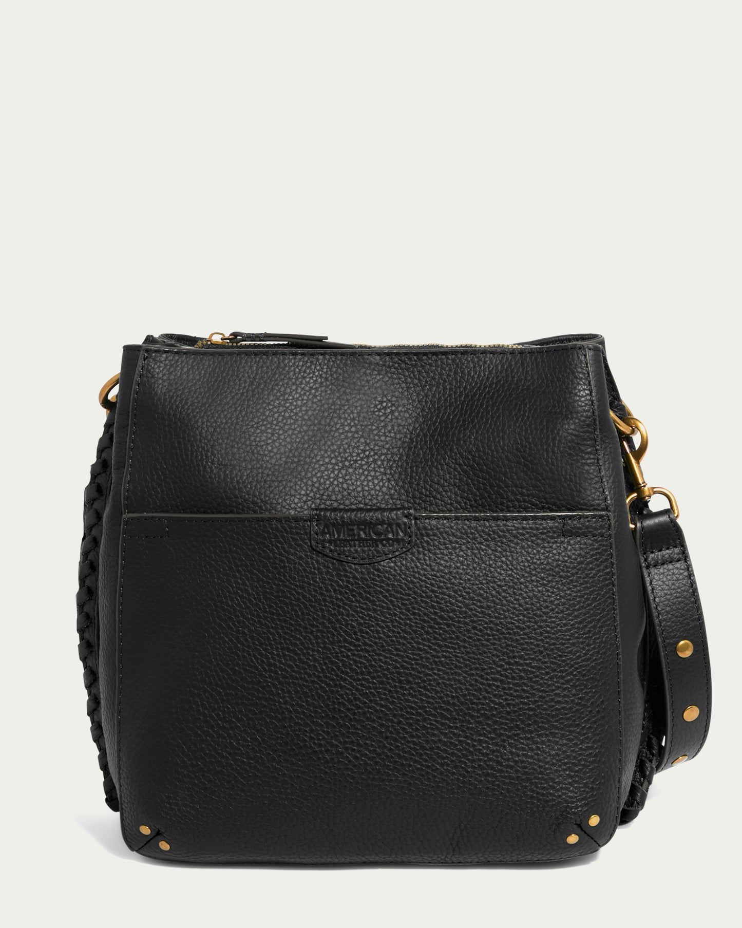 The Luca Triple Entry Crossbody by American Leather Co. is a black leather crossbody bag showcasing a pebbled texture. It features a front pocket, gold hardware, and intricate braided details on the sides. The adjustable strap is adorned with gold studs, while the brand's name and logo are elegantly embossed on the front pocket for an added touch of sophistication.