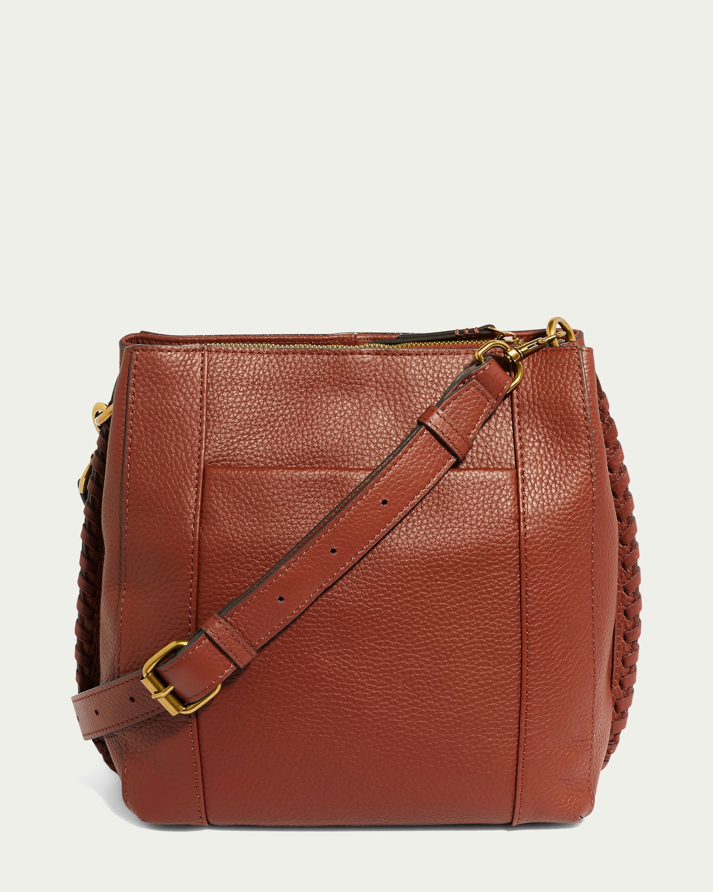 The American Leather Co. Luca Triple Entry Crossbody handbag, displayed upright against a plain light green background, showcases a textured brown leather finish. It features a long, adjustable leather strap with a gold buckle and braided details on the sides, seamlessly combining functionality and elegance.