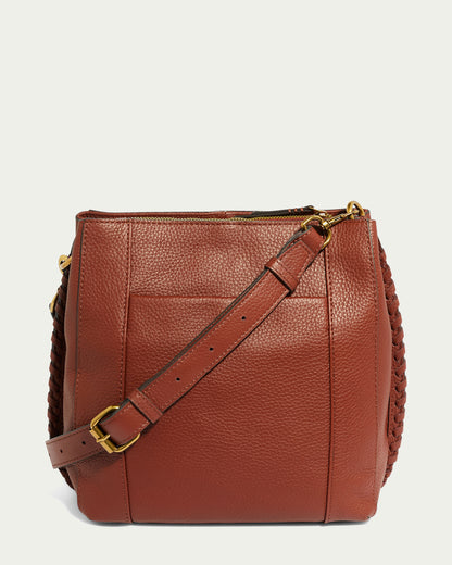 The American Leather Co. Luca Triple Entry Crossbody handbag, displayed upright against a plain light green background, showcases a textured brown leather finish. It features a long, adjustable leather strap with a gold buckle and braided details on the sides, seamlessly combining functionality and elegance.