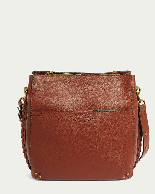 The Luca Triple Entry Crossbody by American Leather Co. is a brown leather bag with a front pocket and a woven strap. It features antiqued goldtone hardware, including rivets and a zipper closure at the top. Crafted from grainy glove-tanned pebble leather, the rectangular-shaped bag has an embossed logo on the front pocket.