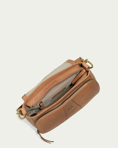 A top-down view of an open Marino Crossbody with 2 Straps handbag by American Leather Co., crafted from butter-soft leather with a beige interior lining. The bag features gold hardware, multiple zippered compartments, and a front pocket. Inside, it contains a small leather label, a side zipper pocket, and an open pouch.