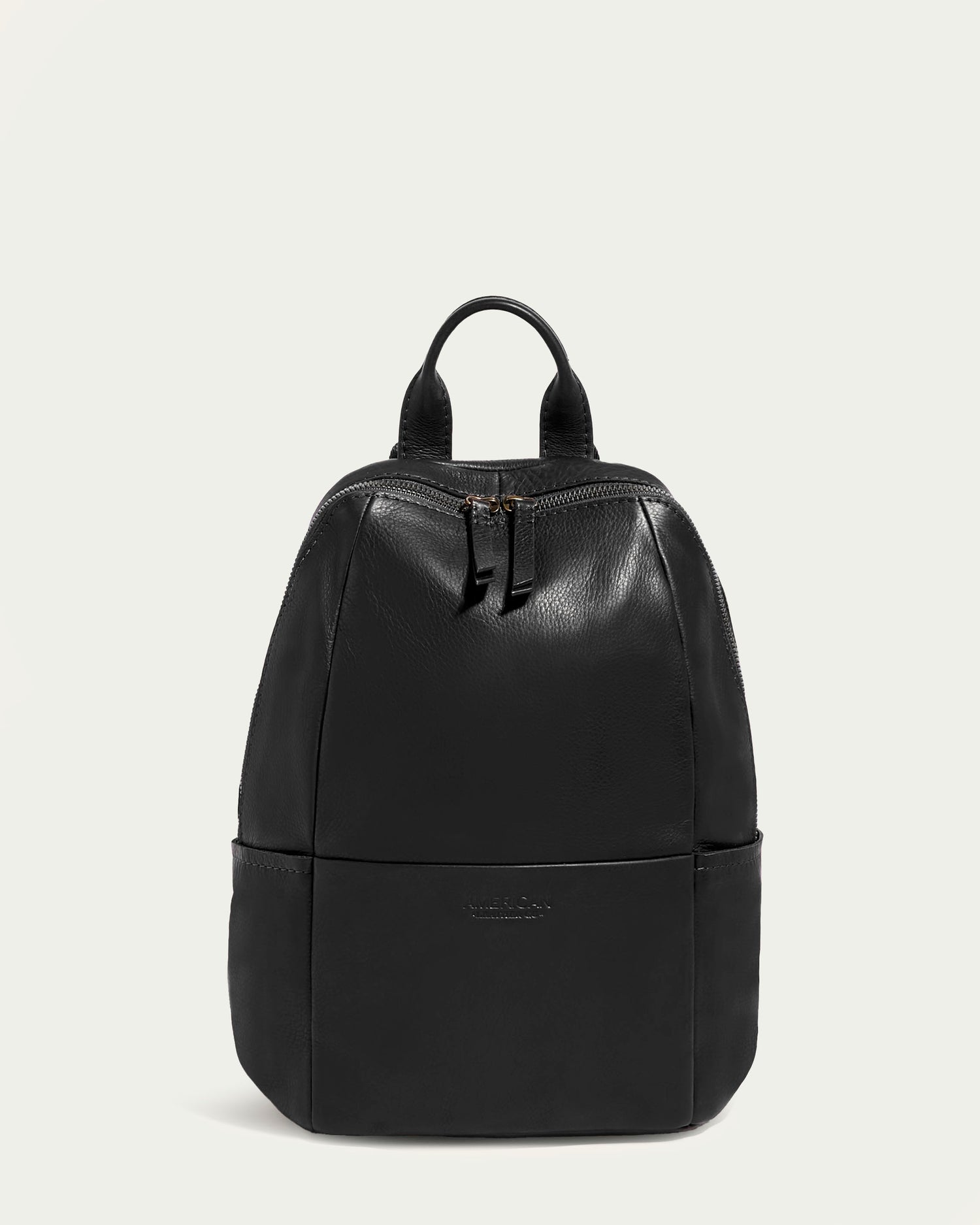 A Melrose Medium Backpack by American Leather Co., crafted in sleek black glove-tanned leather, is showcased against a plain light background. The backpack includes a top handle, adjustable backpack straps, and two front zippers, exuding an elegant and modern appearance with its smooth and polished finish.