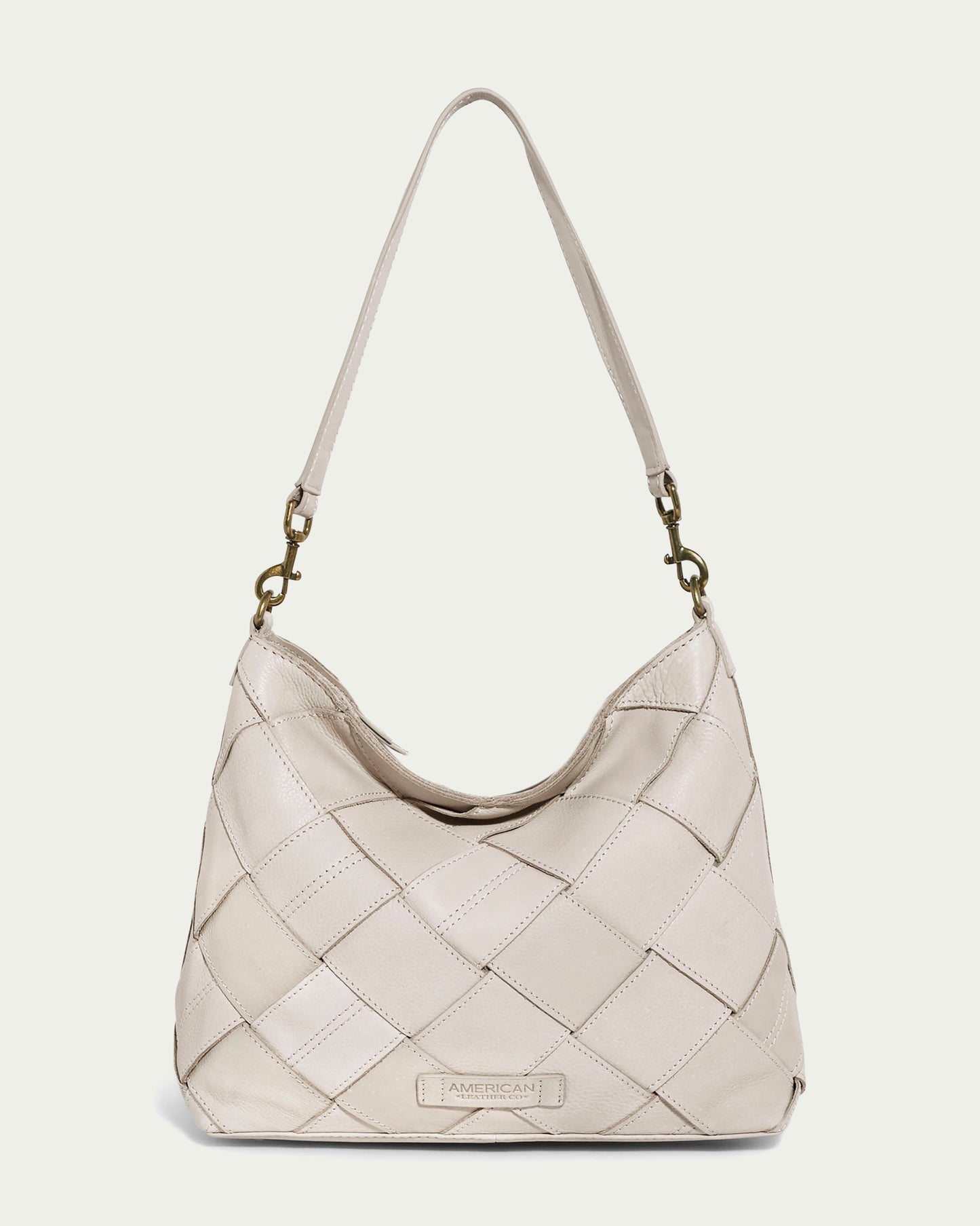 The Mercer Woven Top Zip Hobo by American Leather Co. in ecru exudes timeless elegance with its quilted design and single shoulder strap. It features metal clasps, a discreet logo at the bottom center, and a practical zip-top closure, beautifully combining style and functionality.