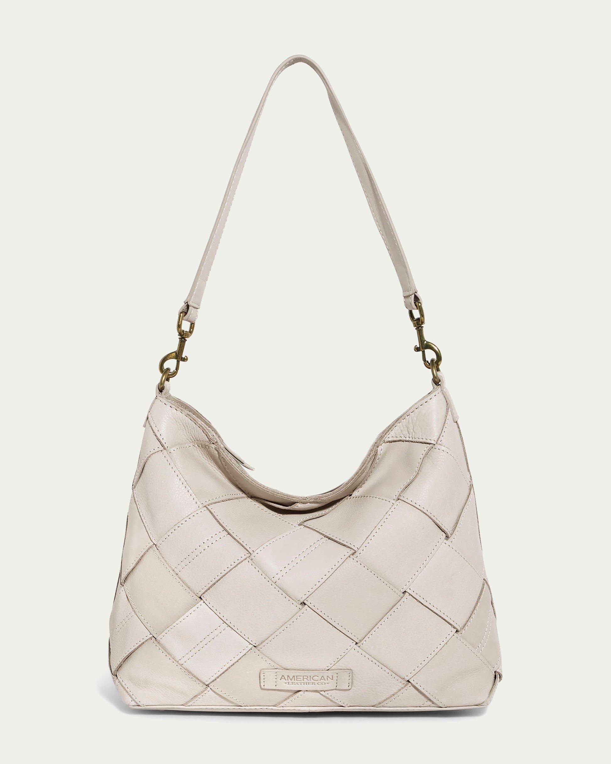 The Mercer Woven Top Zip Hobo by American Leather Co. in ecru exudes timeless elegance with its quilted design and single shoulder strap. It features metal clasps, a discreet logo at the bottom center, and a practical zip-top closure, beautifully combining style and functionality.