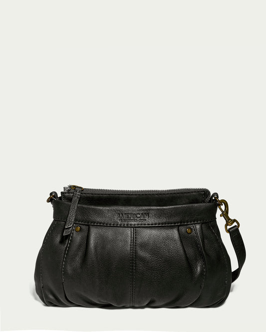 A small Saratoga Crossbody in black, made from Genuine Glove Leather, features a zippered top and an adjustable strap. The bag includes decorative stitching, metal rivet details, and the "American Leather Co." brand embossed on the front. The background is plain and light-colored.