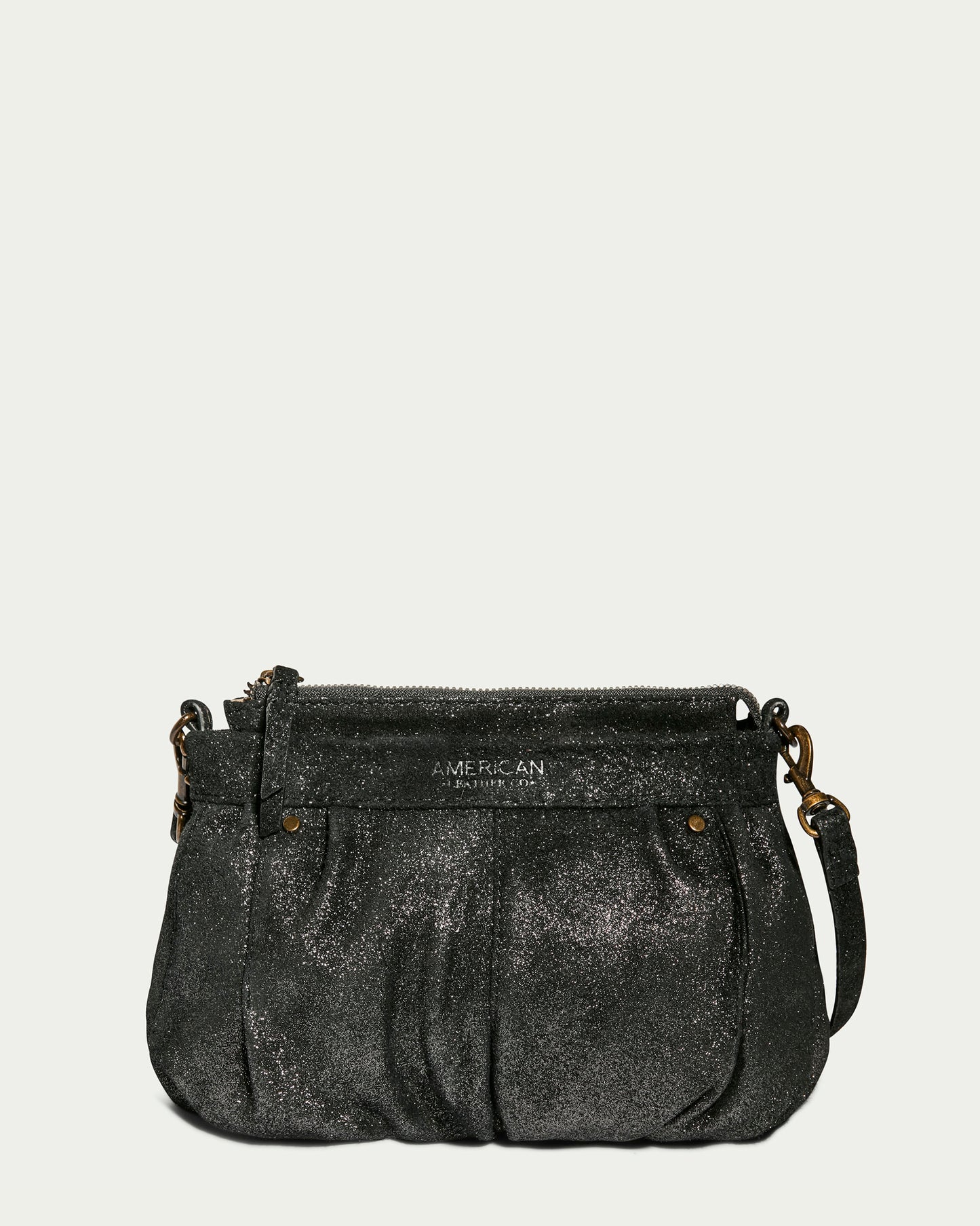 A compact, sparkly black Saratoga Crossbody bag from American Leather Co. featuring a gathered, ruched texture. It is adorned with brass hardware, has a top zipper closure, and comes with a detachable, adjustable crossbody strap. The brand name "American Leather Co." is subtly visible on the front against a plain light gray background.