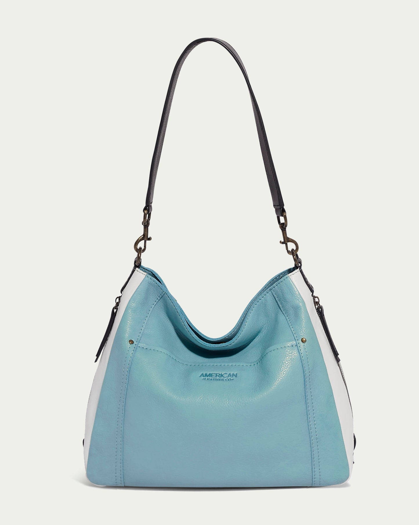 The Austin Shoulder by American Leather Co. is a chic accessory showcasing two-toned light blue and white panels made from authentic American leather. It features a dark brown shoulder strap, a subtly embossed logo, and a slouchy hobo shape, making it an ideal casual piece accentuated by its unique metal hardware.