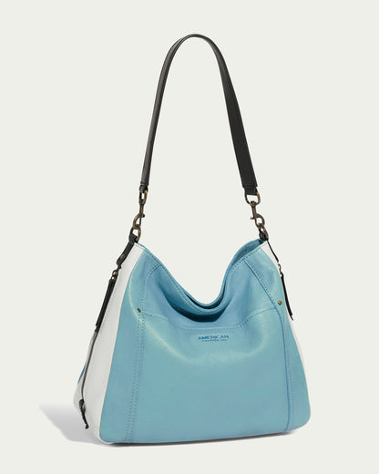 The Austin Shoulder handbag by American Leather Co. is a chic accessory with a striking light blue front and sleek white sides, complemented by an elegant long dark strap. Made from genuine American leather, it boasts a contemporary curved design with a discreet logo centered on the blue panel.