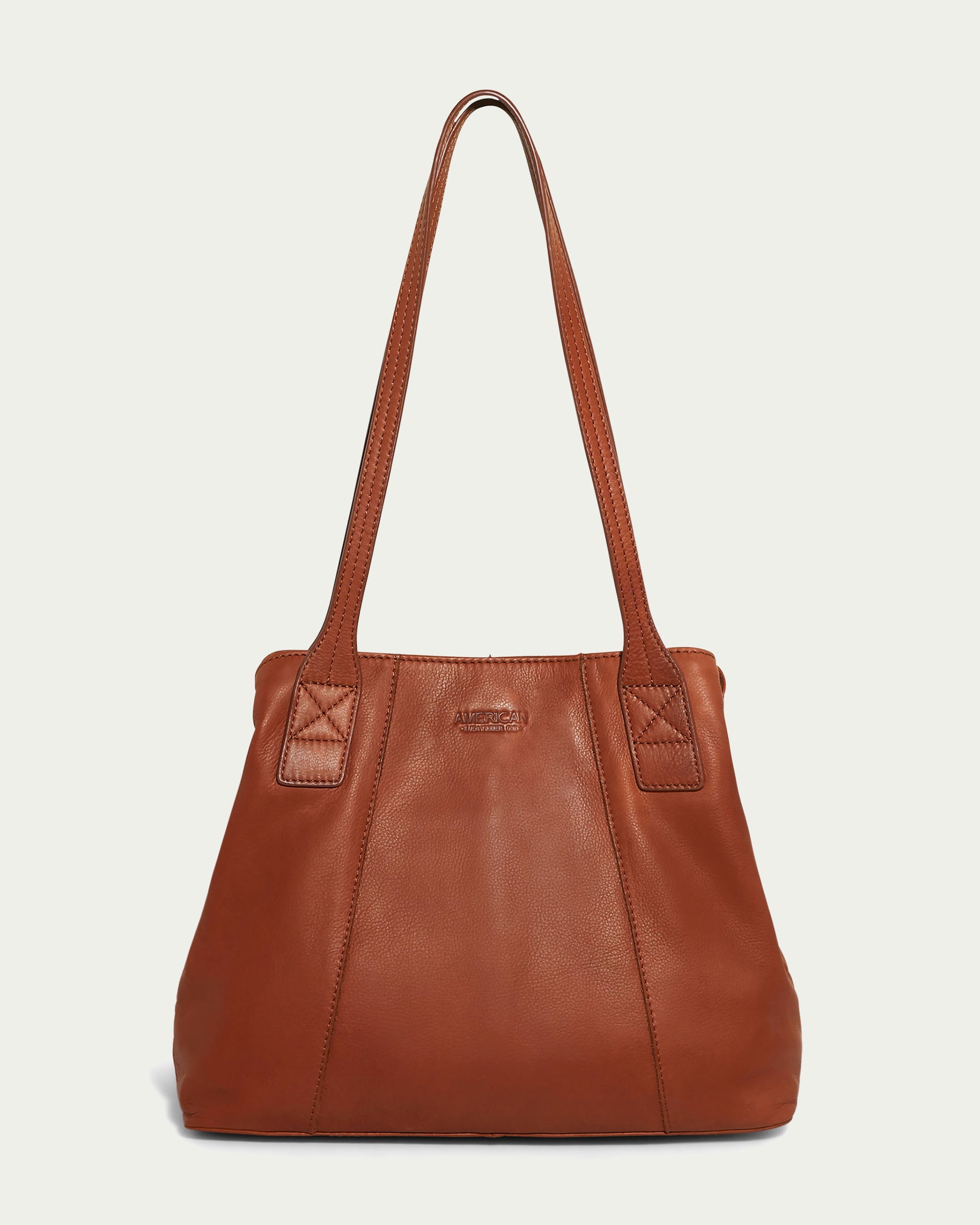 The Ada Triple Entry Tote by American Leather Co. is a stylish brandy-colored leather bag with a smooth texture and two medium-length handles. It features a simple and elegant design with minimal stitching, a subtle brand logo embossed in the center near the top, and excellent interior organization to keep your essentials neatly arranged.