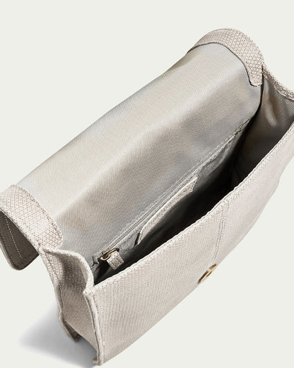 The American Leather Co. Brook Flap Crossbody, an open beige fabric purse, unveils its inner lining and zippered pocket. It features a simple, elegant design with a button clasp and an adjustable strap for versatile wear.