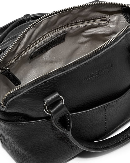 A sleek black handbag crafted from genuine leather, the Carrie Mini Dome Crossbody by American Leather Co. showcases a partially open top zipper that reveals a sophisticated gray interior lining. It features sturdy handles, an adjustable strap, and the brand's embossed name prominently displayed on the exterior. Inside, you'll find a convenient zippered pocket for added functionality.