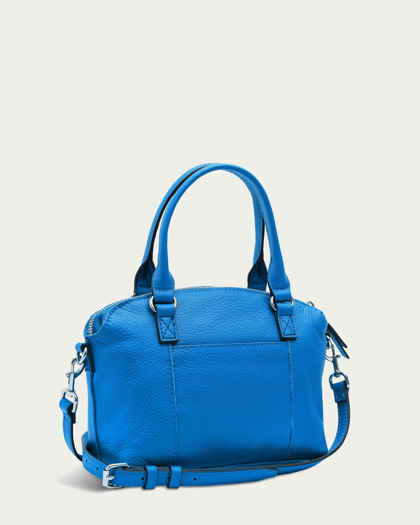 Introducing the Carrie Mini Dome Crossbody by American Leather Co., a vibrant blue genuine leather handbag adorned with silver hardware. This stylish accessory features two sturdy handles, an adjustable and detachable shoulder strap, a zippered main compartment, multiple pockets for organization, and visible stitching details that enhance its chic and functional design.