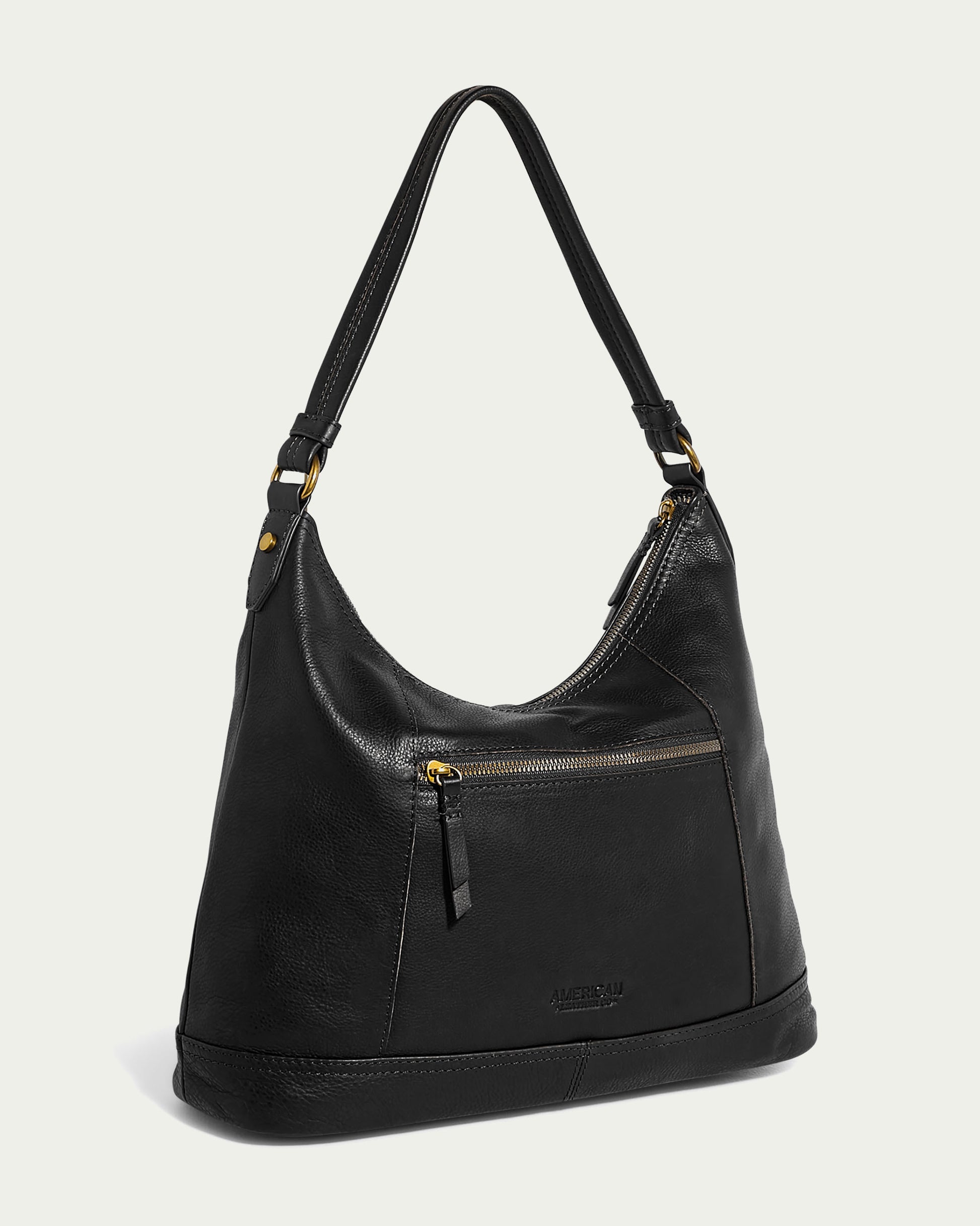 The Evelyn Hobo by American Leather Co. is a black leather handbag with a single shoulder strap and gold-tone hardware. This luxury hobo bag features an external front zipper pocket with a black leather pull tab and detailed stitching. The brand logo is embossed near the bottom of this genuine leather accessory.