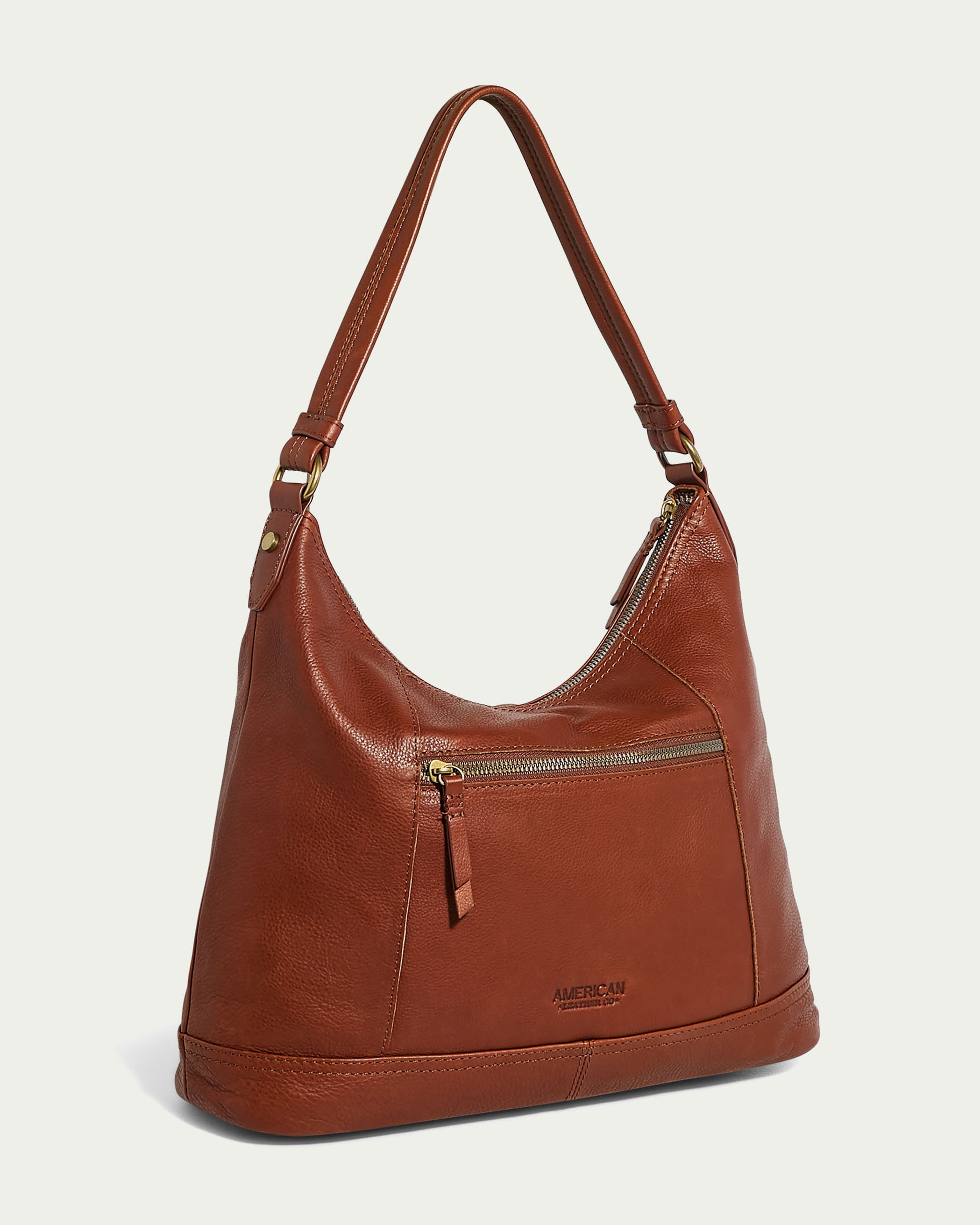 The Evelyn Hobo by American Leather Co. is a stylish brown leather shoulder bag with a single strap and gold-tone hardware. It features a front zipper pocket, subtle stitching, and "American Leather Co." embossed near the bottom of the front pocket.