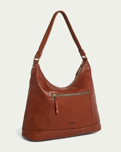 The Evelyn Hobo by American Leather Co. is a stylish brown leather shoulder bag with a single strap and gold-tone hardware. It features a front zipper pocket, subtle stitching, and "American Leather Co." embossed near the bottom of the front pocket.