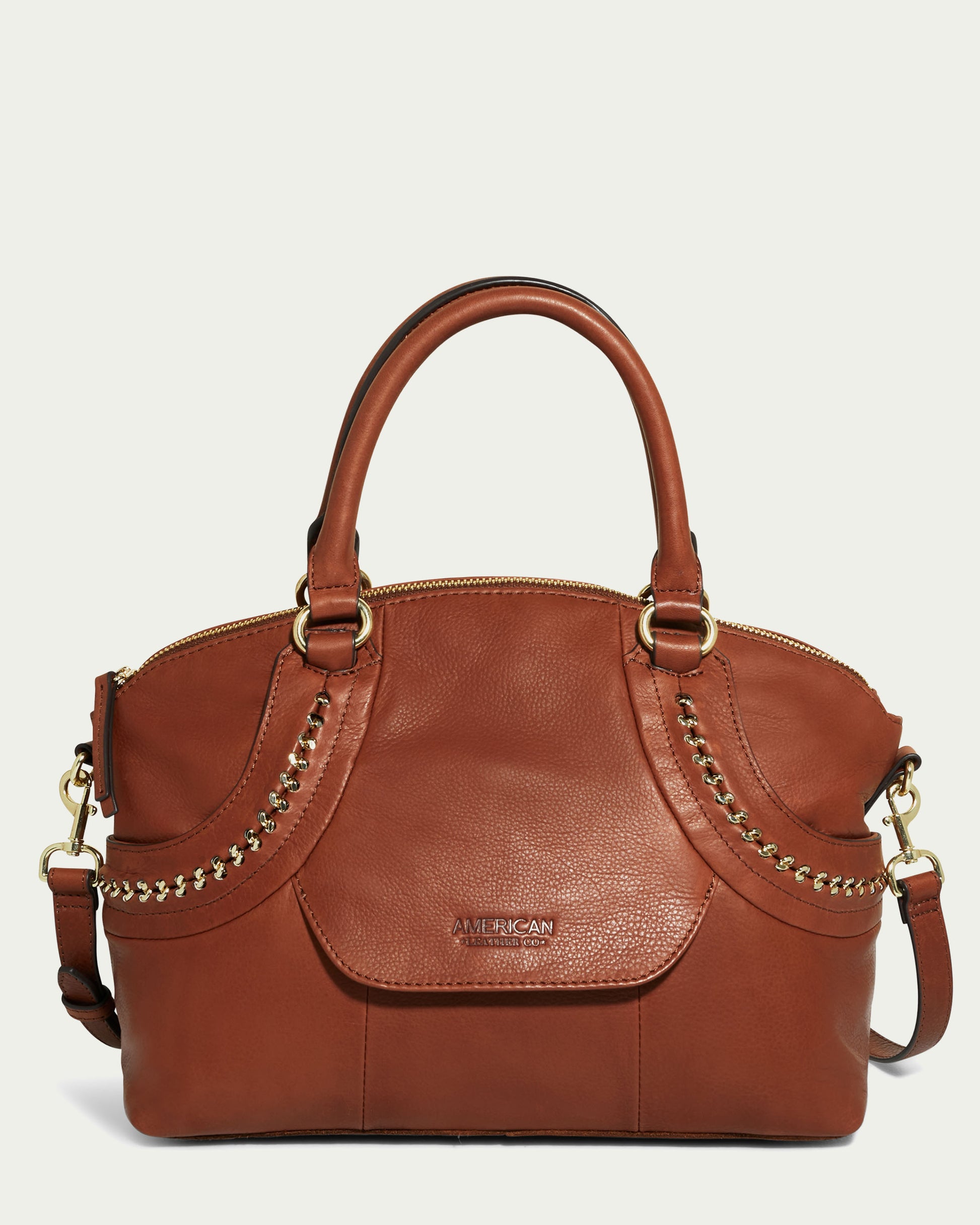 The Janssen Dome Satchel by American Leather Co. is a brown leather handbag featuring gold chain detailing on the sides. It has a rounded top handle, a detachable shoulder strap, and a front pocket. The front of this genuine leather accessory is embossed with the brand logo.