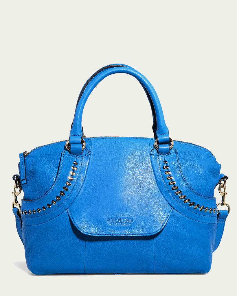 A vibrant blue Janssen Dome Satchel by American Leather Co., crafted from genuine leather and adorned with gold chain accents and two handles. The bag features a front flap embossed with the brand name against a light, solid background.