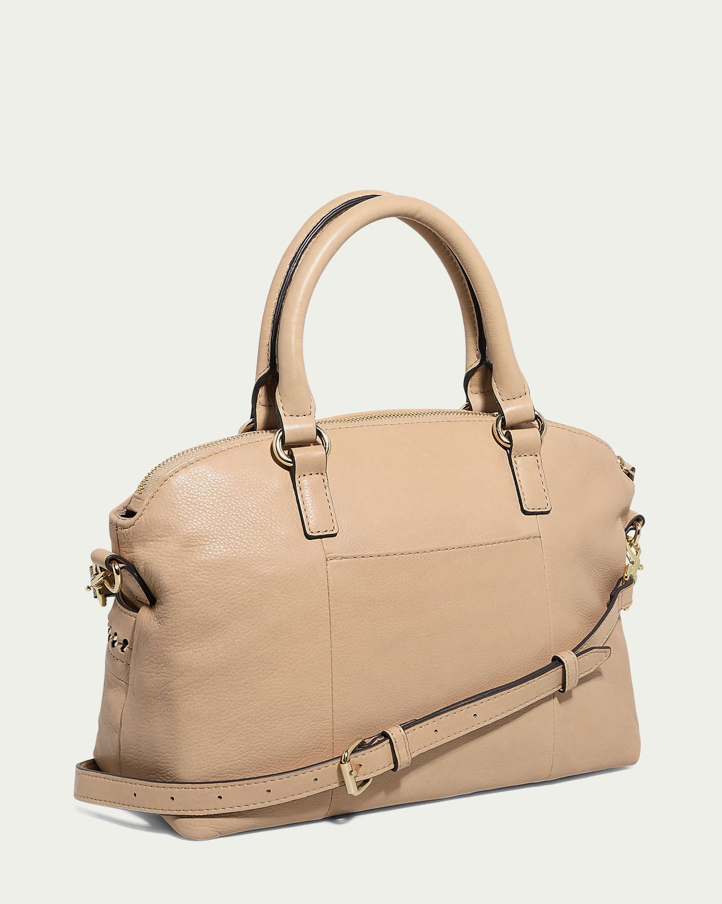 Against a plain light background, the Janssen Dome Satchel by American Leather Co. is featured, showcasing its sleek rectangular design. This beige leather handbag includes two short handles, a detachable shoulder strap, gold-tone hardware, and a zip closure for everyday elegance.