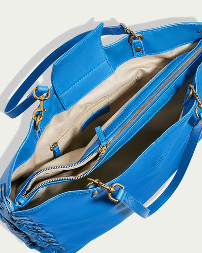 A top-down view of the Lenox Triple Compartment Tote by American Leather Co. in bright blue leather with gold hardware. The bag is open, revealing a beige interior with multiple compartments, including a zippered pocket and a pouch, showcasing its triple entry compartment design. This genuine leather tote features shoulder straps and decorative stitching on the exterior.