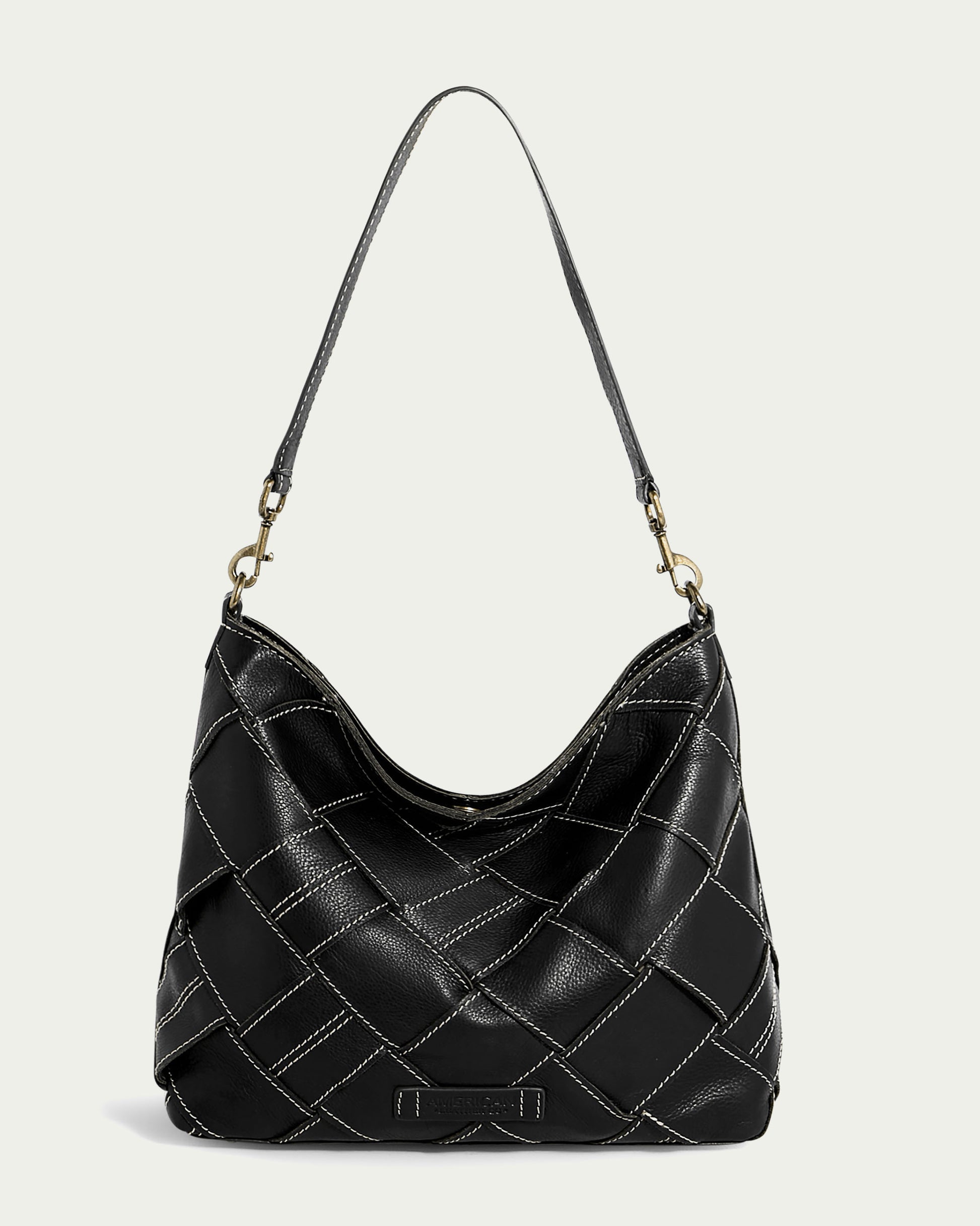 Experience the chic design of the Mercer Shoulder handbag by American Leather Co. Crafted in black genuine leather, this bag boasts a quilted pattern complemented by white stitching. It features a detachable single shoulder strap connected with gold hardware and a subtly rounded top, all set against a plain, light grey background.