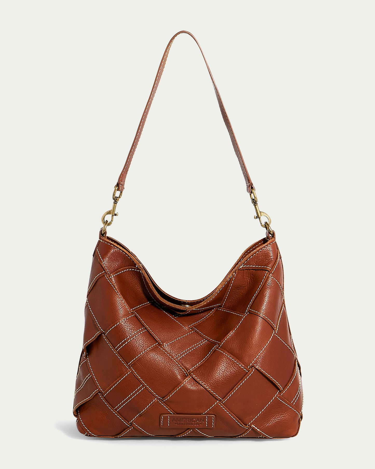 A genuine brandy leather handbag with a quilted pattern on the front. The Mercer Shoulder bag from American Leather Co. features a single shoulder strap attached with gold hardware and a small leather patch at the bottom center with an embossed brand logo, set against a plain off-white background.