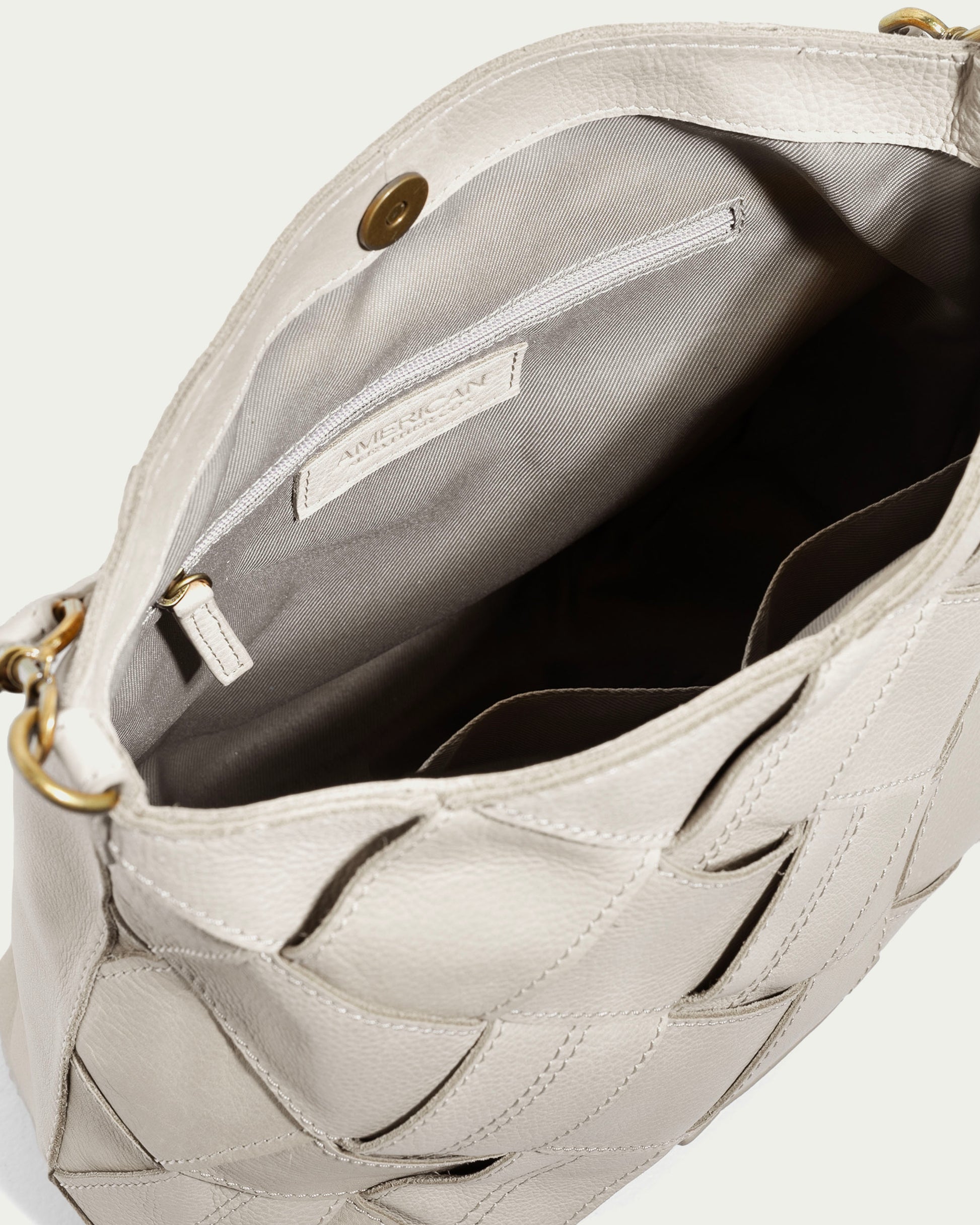 The Mercer Shoulder handbag by American Leather Co. is displayed in an open beige design featuring genuine leather with a woven pattern. Inside, it boasts a fabric lining and a zippered pocket. The bag includes gold hardware, a detachable strap, and seems to offer plenty of interior space.