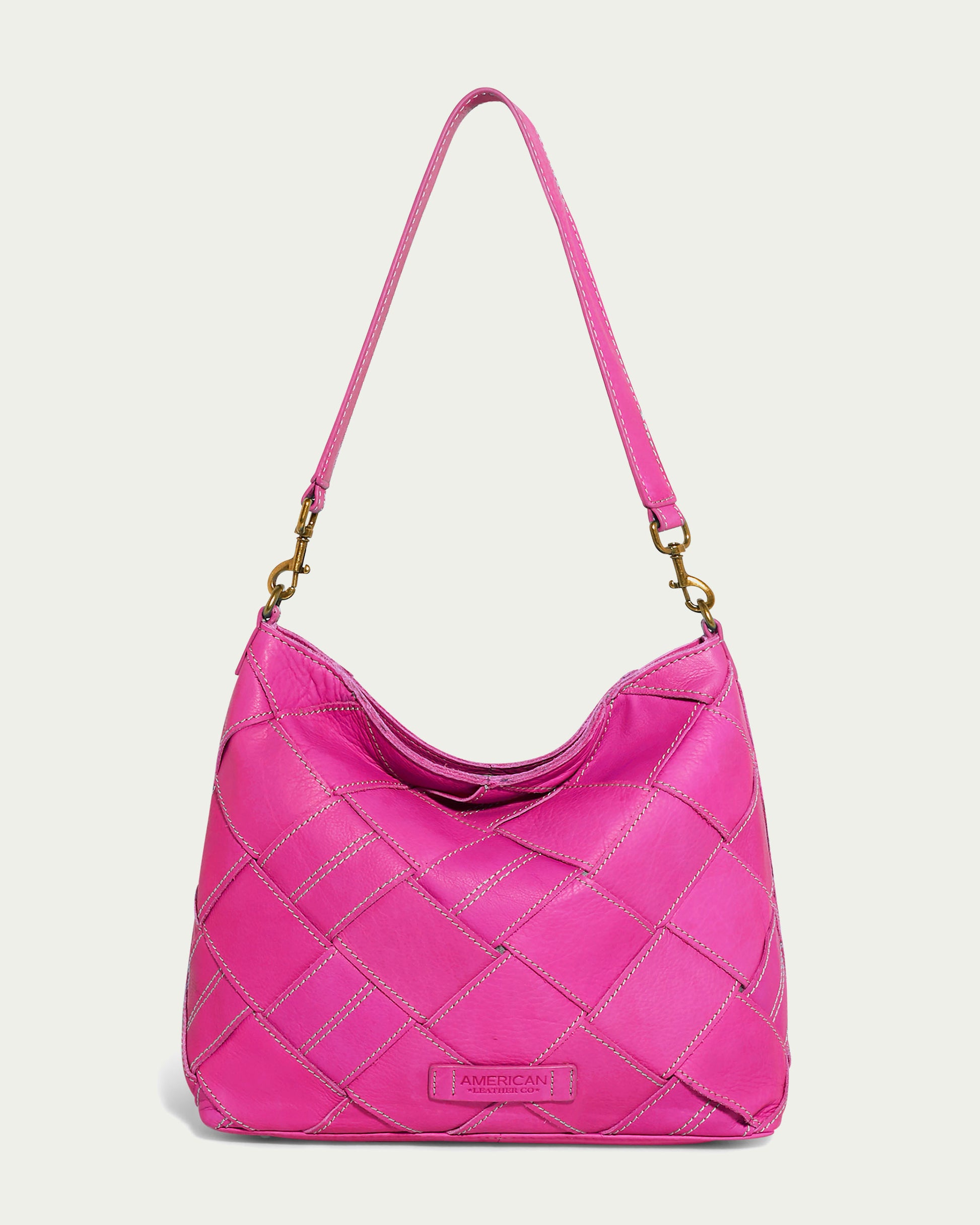 The American Leather Co. Mercer Shoulder bag in vibrant Knockout Pink woven genuine leather features a single strap with gold clasp attachments, displayed against a plain off-white background. Additionally, it comes with a detachable shoulder strap for versatile styling.