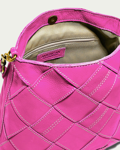 A close-up of the stylish Mercer Shoulder handbag in pink, showcasing its textured, quilted pattern with white stitching. The handbag is open, revealing a beige interior that includes a zippered pocket. The label inside reads "American Leather Co." Made of genuine leather, the bag features gold hardware, a clasp closure, and comes with a detachable shoulder strap.