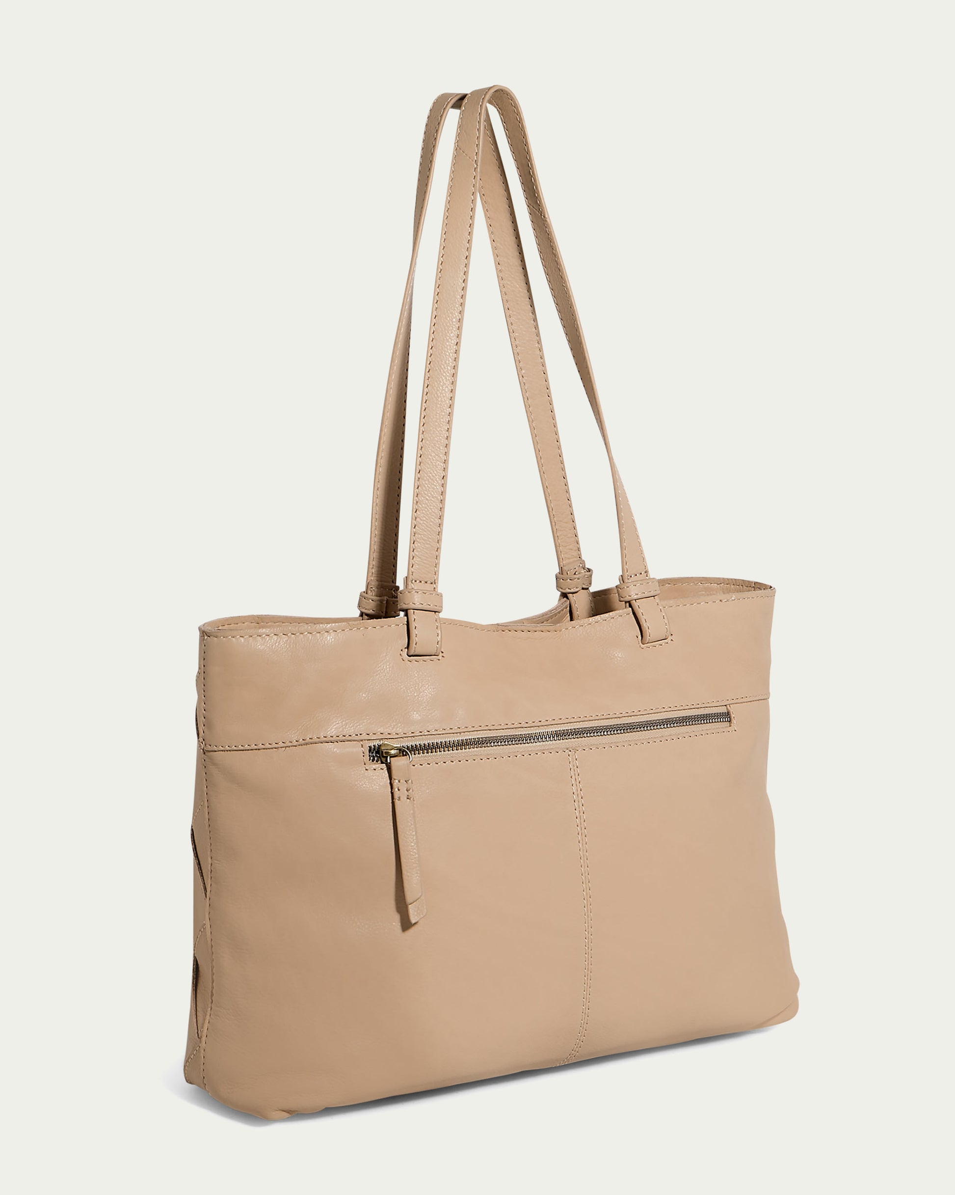 The Mercer Woven Tote, a creation of American Leather Co., is a beige tote bag made from genuine leather. It showcases two long handles and a front zipper pocket, set against a light background to highlight its soft texture and elegant, minimalist design.