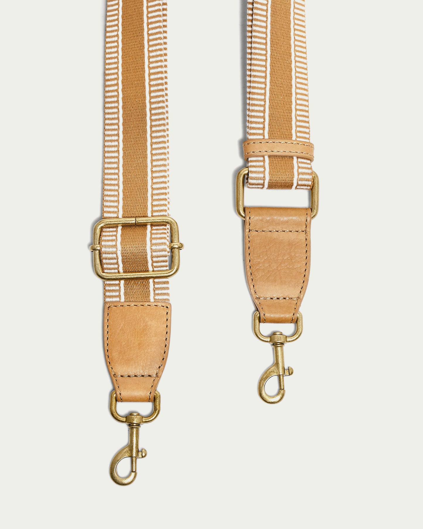 A close-up of the Striped Web Strap by American Leather Co. showcases its beige and white striped design, complete with antiqued hardware, gold-tone buckles, and swivel hooks for easy attachment to bags or accessories.