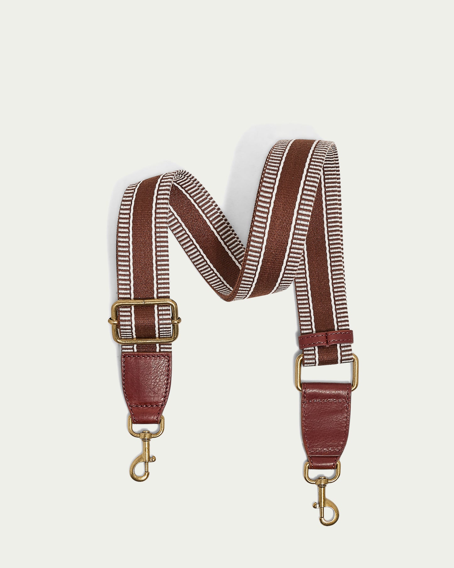 The Striped Web Strap by American Leather Co., showcasing brown and white stripes, adjustable antiqued gold buckles and clips, and dark brown leather ends, is elegantly displayed on a light background.