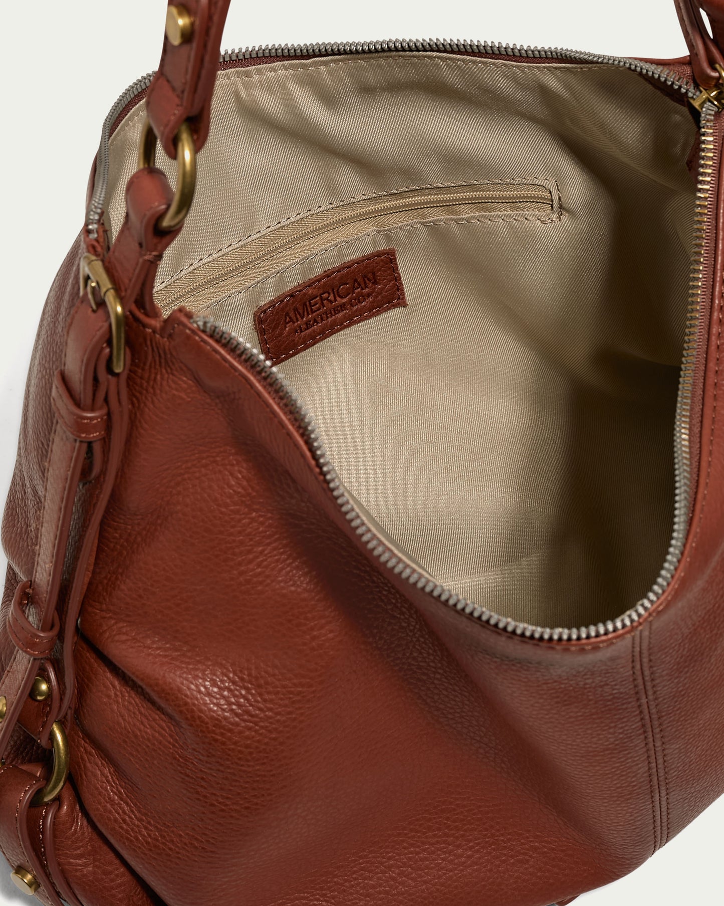 A close-up image of an open brown leather Thayer Perfect Hobo handbag with a beige interior lining. The bag, made from genuine leather, features a zipper closure, brass hardware, and a small interior pocket with a leather patch label reading "American Leather Co.