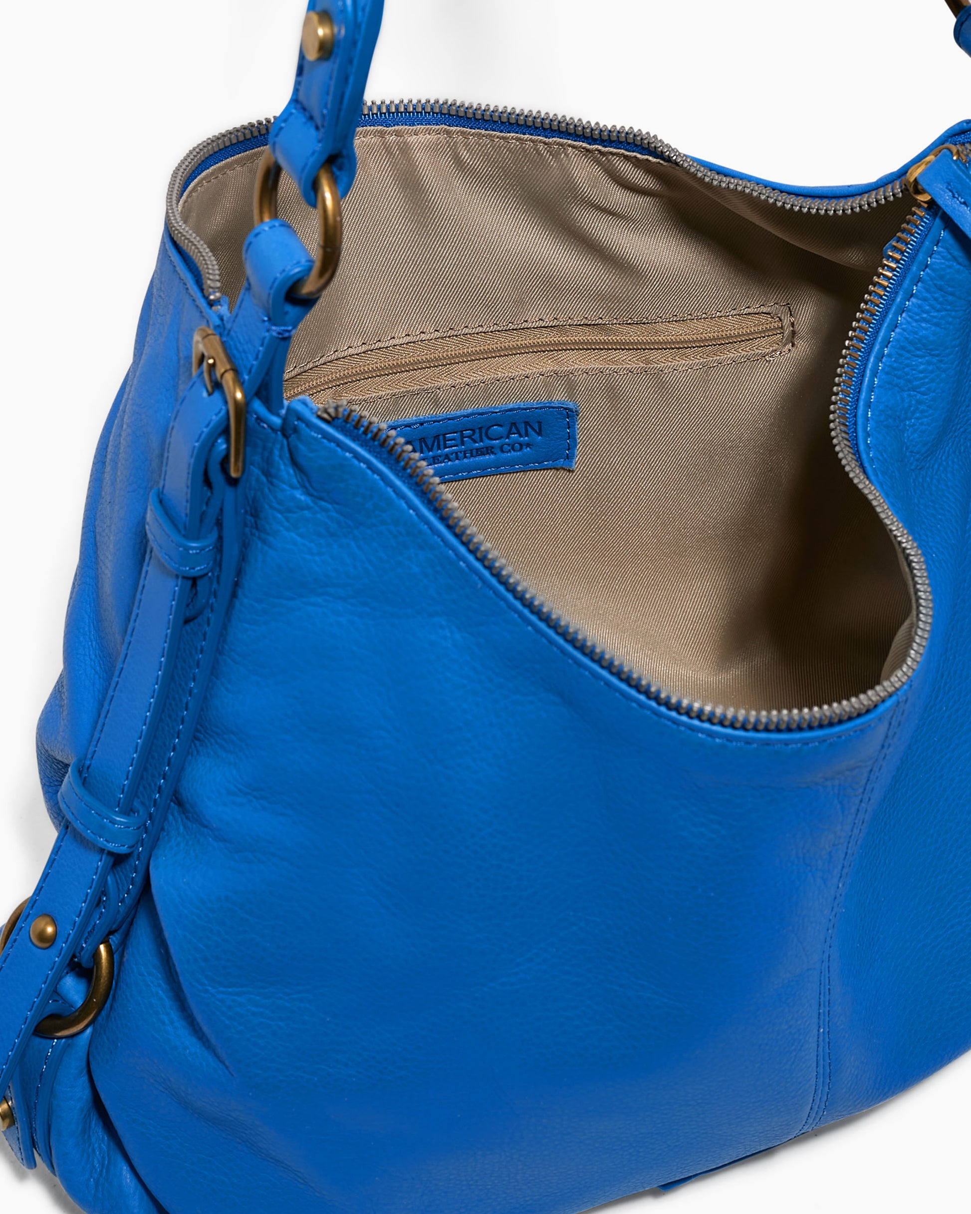 Open blue leather Thayer Perfect Hobo by American Leather Co., crafted from genuine leather with a beige interior. It features adjustable shoulder straps with metal rings, a zip closure, and a visible brand label inside.