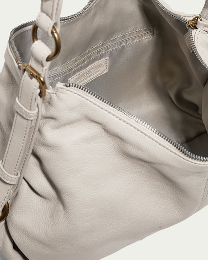 A close-up of the American Leather Co. Thayer Perfect Hobo in light-colored genuine leather reveals a visible zipper pocket inside. This leather purse is adorned with gold-tone hardware, including rings that attach the strap. The interior looks spacious and features a soft fabric lining.