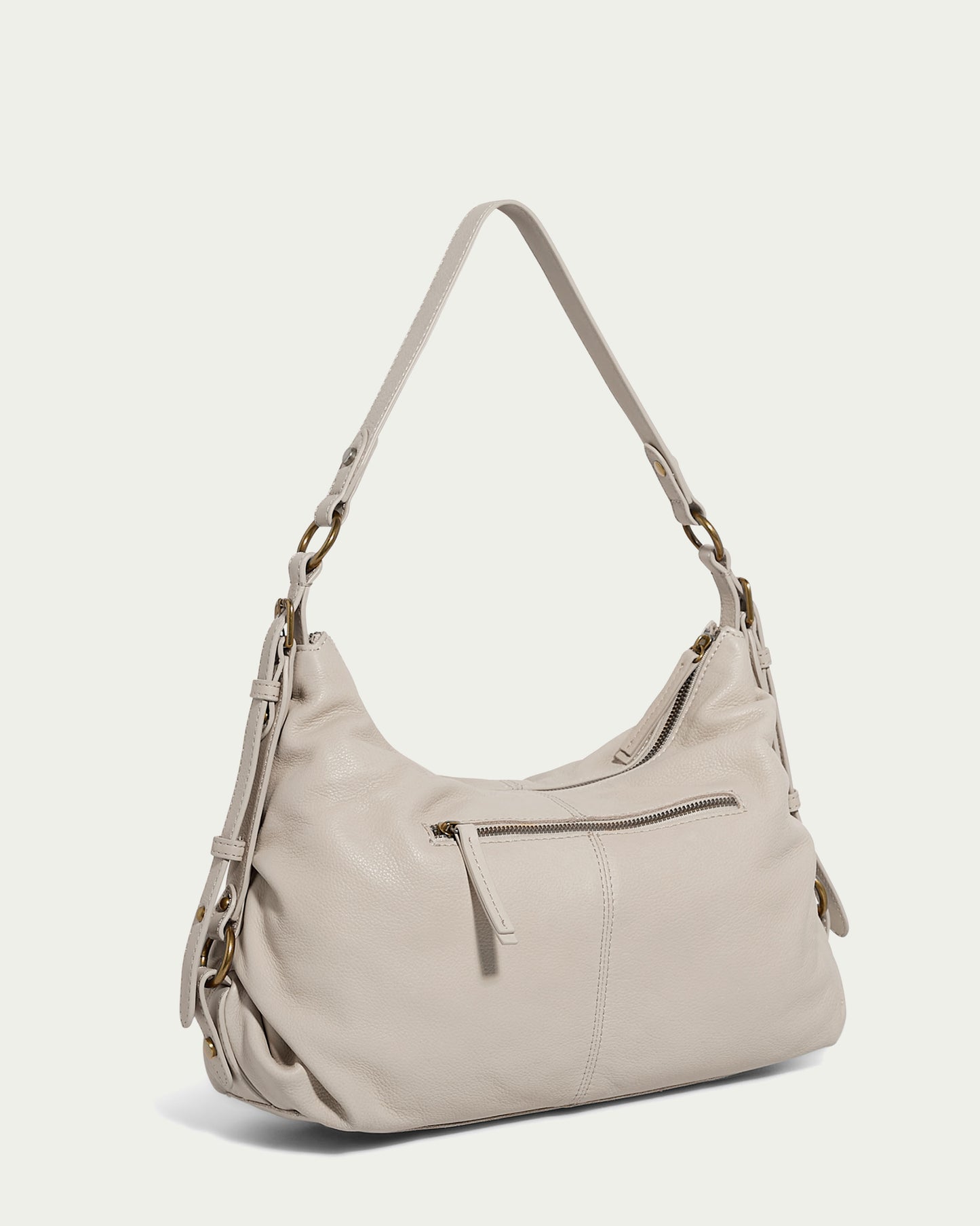 The Thayer Perfect Hobo by American Leather Co. is a light beige leather bag with a curved shape. It features a front zip pocket, two buckled side straps, and a single shoulder strap. This genuine leather purse showcases a minimalist design set against a plain backdrop.