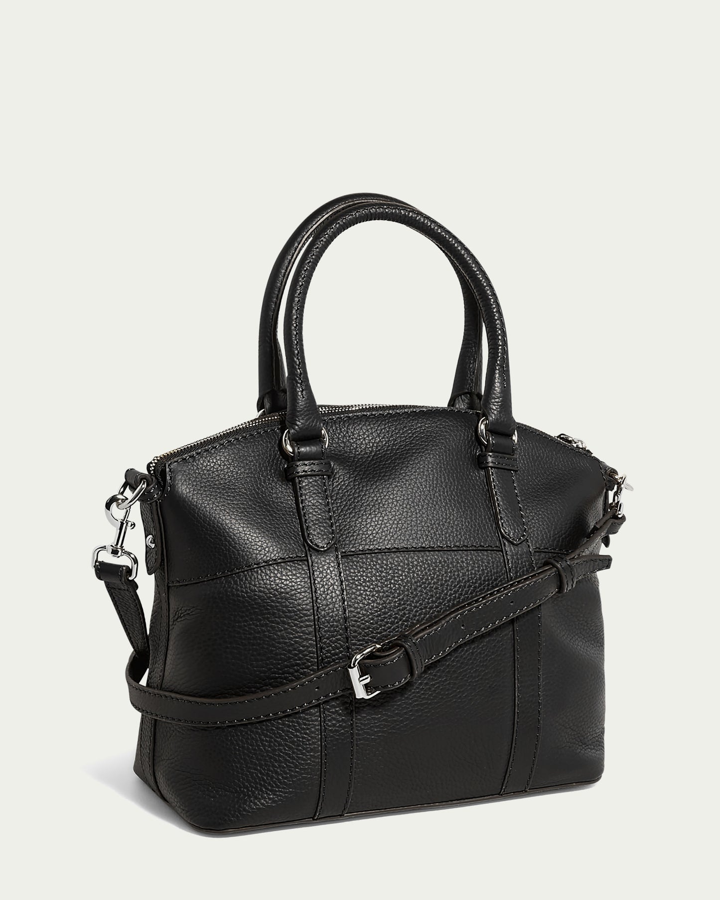 The American Leather Co.'s Vona Convertible Dome Satchel in Forever Pebble leather is a black handbag with a textured surface. It features two short handles and a detachable, adjustable shoulder strap with a silver buckle. The bag is adorned with silver hardware, including zippers and metal clips that attach the strap to the bag.