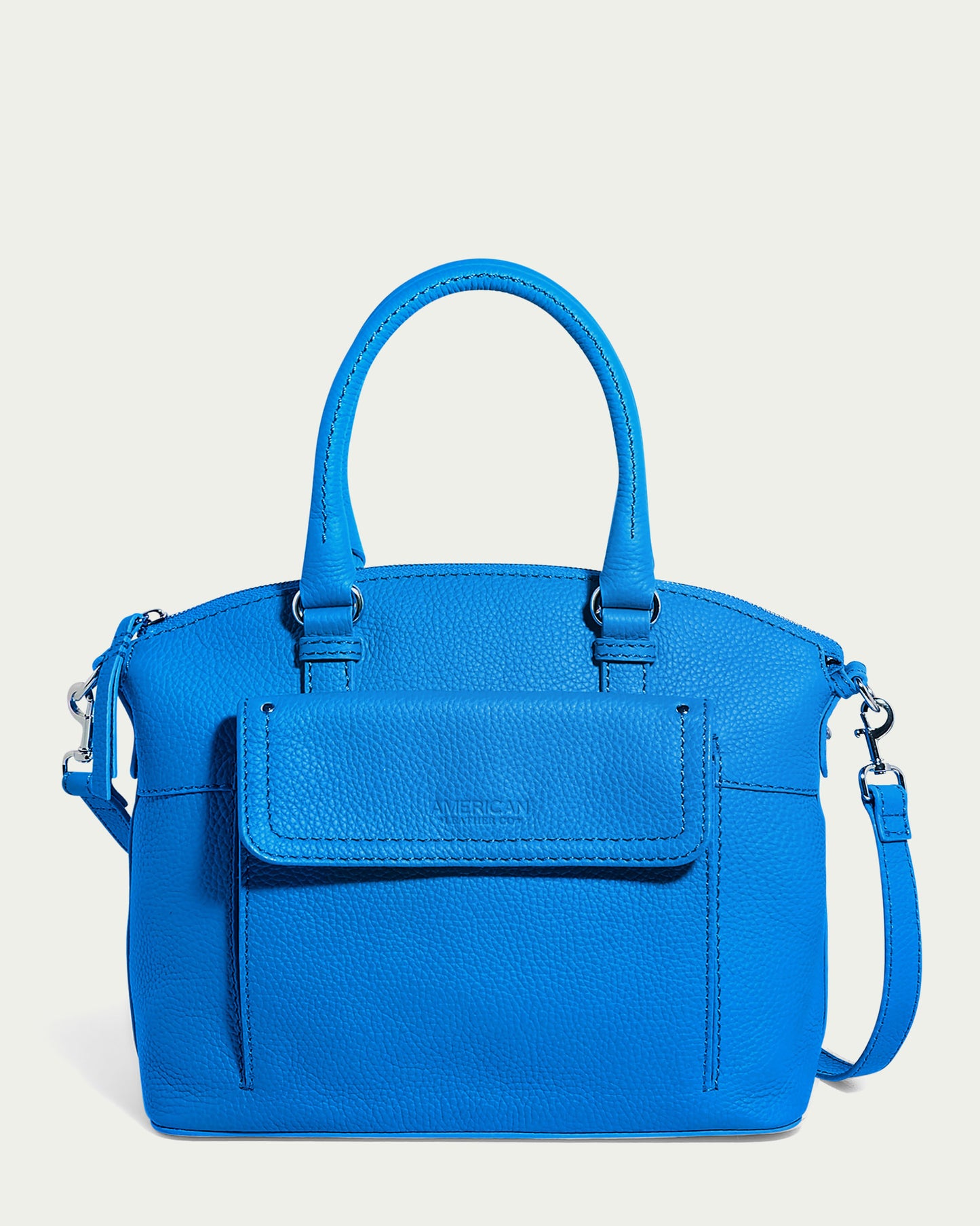 A vibrant cerulean blue pebbled Vona Convertible Dome Satchel by American Leather Co., crafted from genuine leather, with two handles and a detachable shoulder strap. The bag features a front flap pocket and minimal stitching details. The slightly pebbled texture of the leather adds a subtle rugged look.