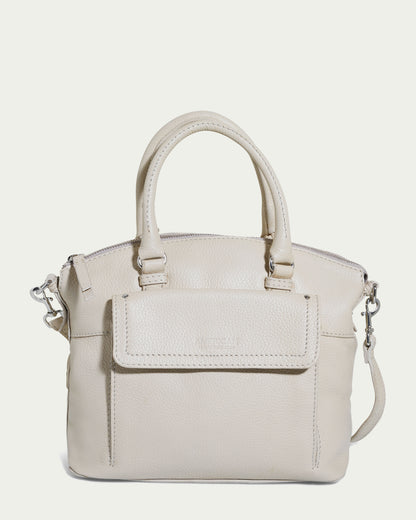 The Vona Convertible Dome Satchel by American Leather Co. comes in a light beige "Ecru Pebble" genuine leather with dual handles and an adjustable, detachable shoulder strap. This handbag features a front flap pocket, zipper closure, and silver hardware, with a smooth texture and slightly pebbled finish.