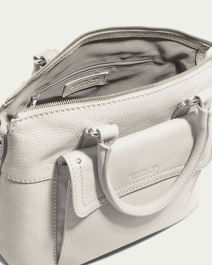 A light gray leather handbag with a textured surface, two short handles, and an open top revealing an interior with a zippered pocket. This Genuine Leather piece by "American Leather Co." features embossed exterior and interior patches, making it the perfect Vona Convertible Dome Satchel for any occasion.