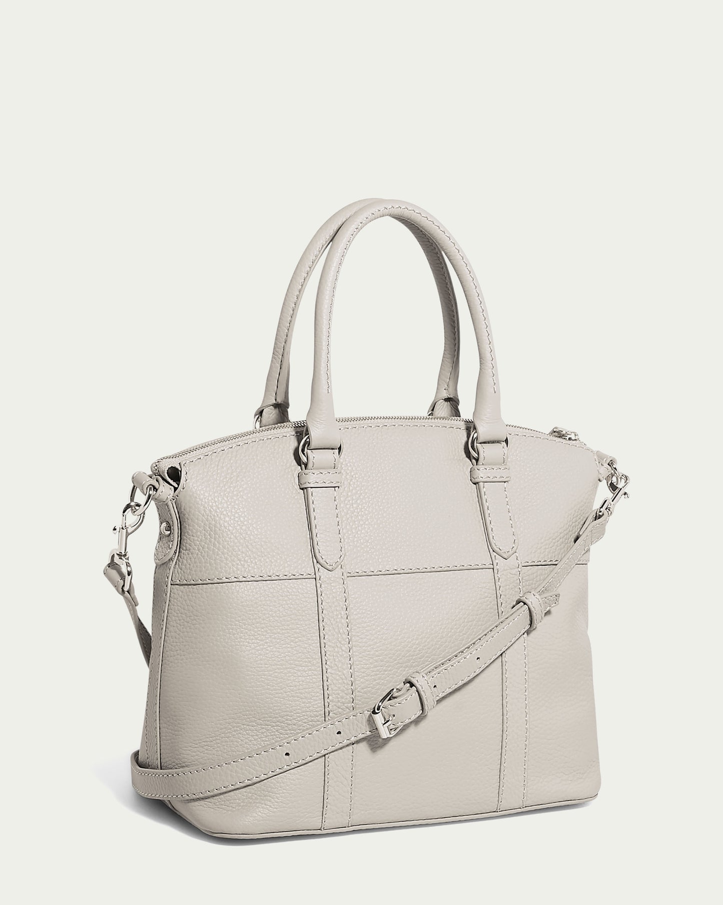 The Vona Convertible Dome Satchel by American Leather Co. is a light gray genuine leather handbag with dual handles and a removable, adjustable shoulder strap. It boasts silver hardware, a structured shape, and stitching details that enhance its elegant design. The plain background ensures the satchel stands out clearly.