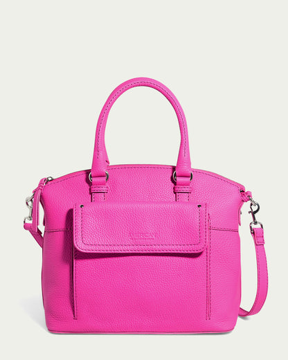 The Vona Convertible Dome Satchel by American Leather Co. is a vibrant Knockout Pink Pebble handbag featuring a detachable shoulder strap and two top handles. It includes a front flap pocket adorned with a subtle embossed brand name, crafted from genuine pebbled leather with silver hardware.