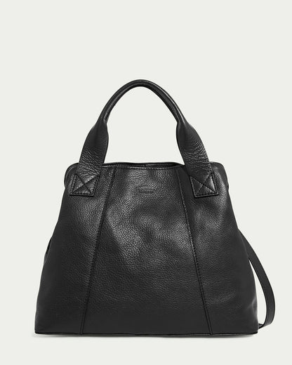 The Ada Triple Entry Satchel by American Leather Co. is a black handbag made of genuine American leather, featuring a smooth texture and simple design with subtle stitching. It has structured handles that pair well with its adjustable crossbody strap and sits against a soft, light backdrop.