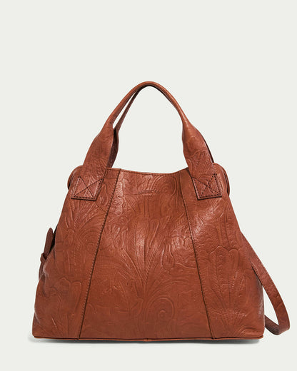 The Ada Triple Entry Satchel by American Leather Co. is a brown leather handbag featuring embossed floral patterns, crafted from Genuine American Leather. It includes sturdy handles and a detachable crossbody strap, shown against a plain white background.