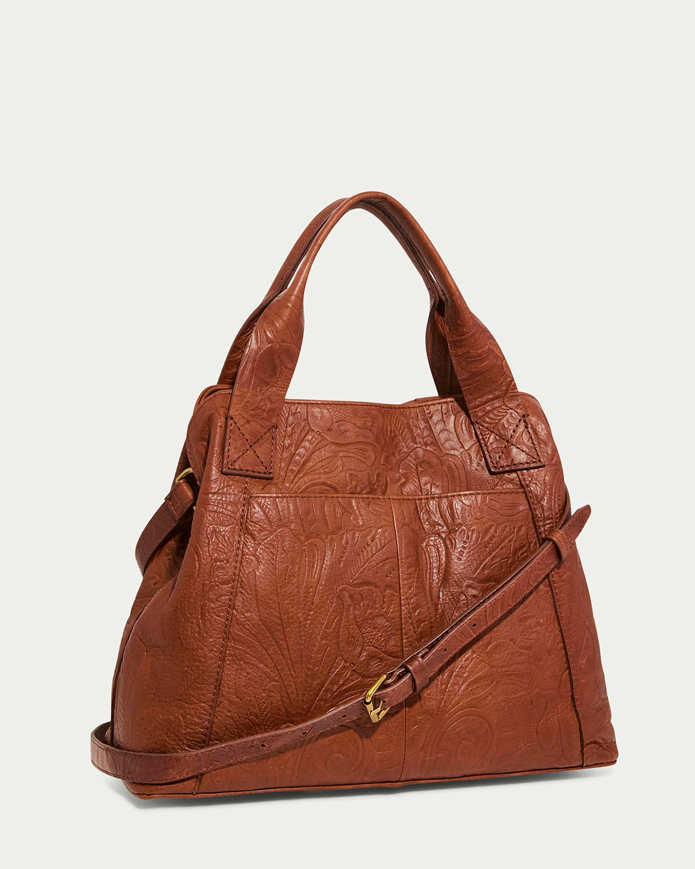 The Ada Triple Entry Satchel by American Leather Co. is made from genuine American leather and features intricate floral patterns. It includes a short handle, a detachable adjustable crossbody strap with a gold buckle, and offers an elegant and textured design.