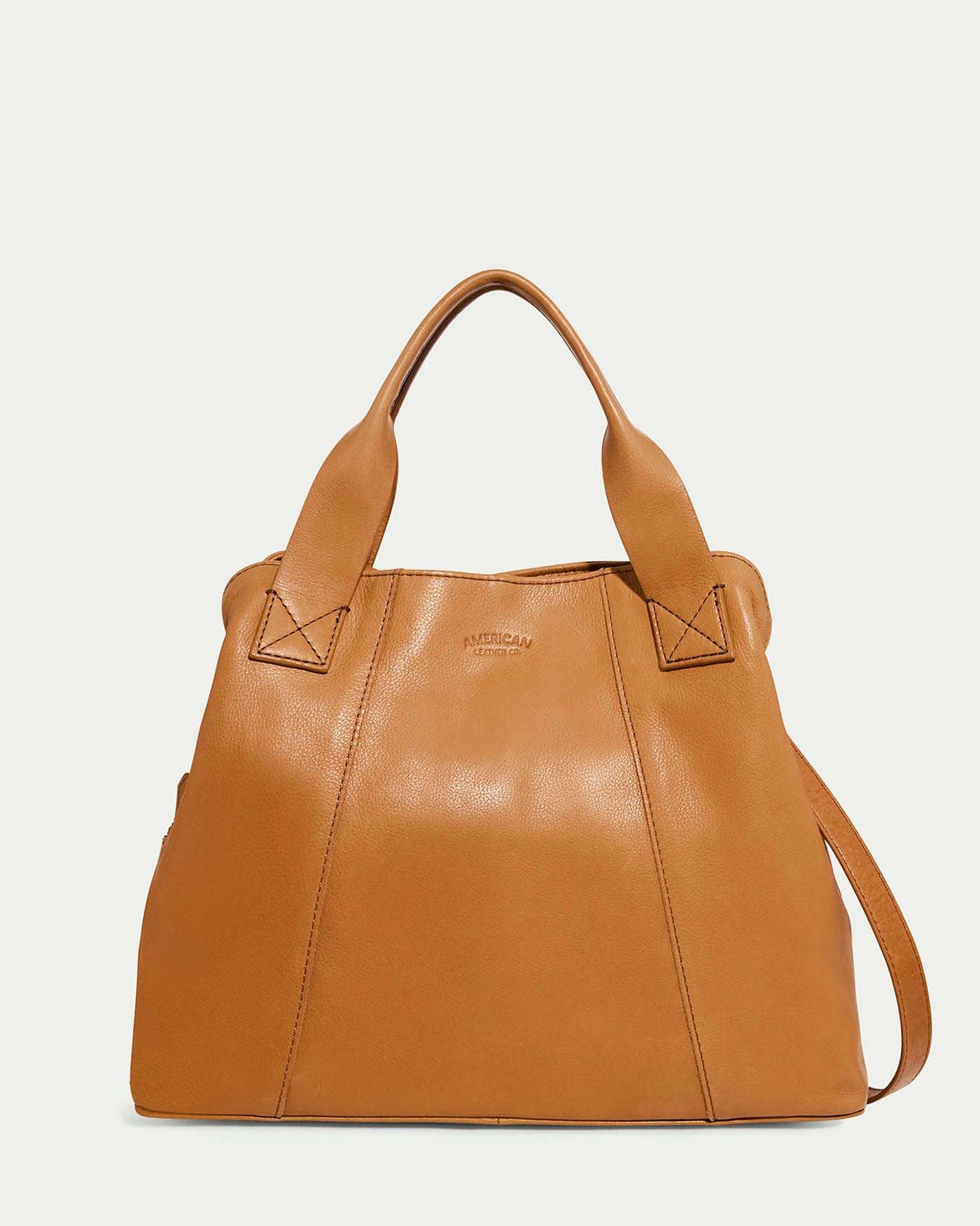 The Ada Triple Entry Satchel by American Leather Co. is a cafe latte colored, structured handbag crafted from genuine leather. It features a smooth texture, two sturdy straps, a subtle embossed logo on the front, and an adjustable crossbody strap for versatile wear.