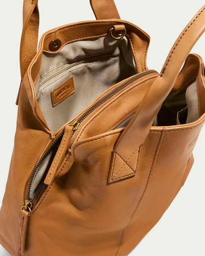 The Ada Triple Entry Satchel by American Leather Co. is a brown leather handbag with two handles and an adjustable strap, standing upright to show its beige interior lining with a zipper pocket and visible stitched leather tag, all set against a plain background.