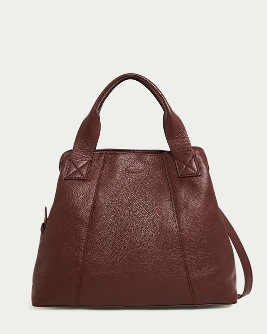 The Ada Triple Entry Satchel by American Leather Co. in cordovan is a genuine leather handbag with a textured surface, two sturdy handles, an adjustable crossbody strap, and detailed stitching near its slightly trapezoidal top.